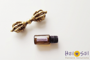 A bottle of doTERRA Patchouli essential oil next to a brass ornamental piece, positioned on a white background with the "Hol Sol Holistic Solutions" logo in the bottom right corner.