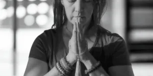 A woman with prayer beads on her wrists holds her hands in a prayer position near her face, appearing to meditate or pray, possibly practicing breathing for anxiety.