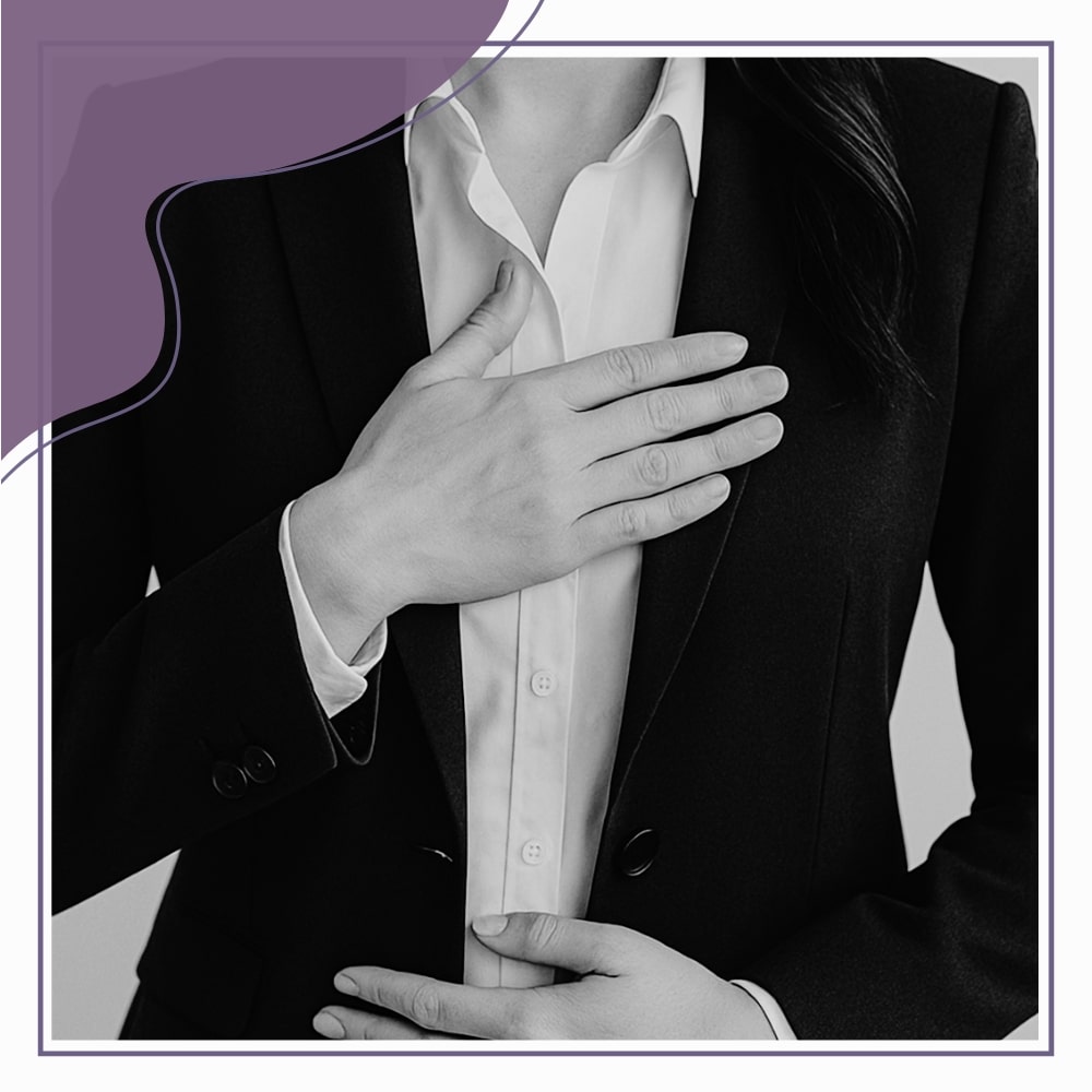 A person in a suit places one hand on their chest and the other on their abdomen, standing against a plain background.
