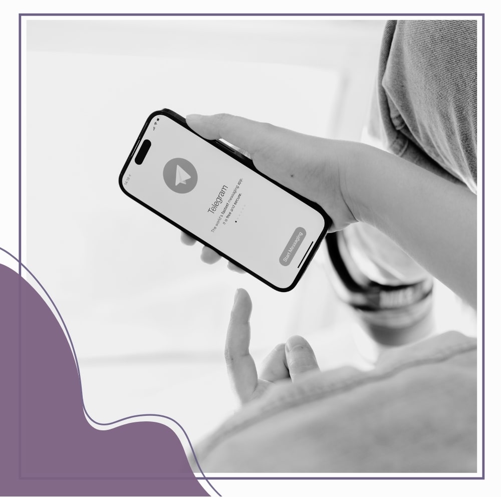 A person holds a smartphone displaying the Telegram app welcome screen, with their finger pointing towards the "Start Messaging" button.
