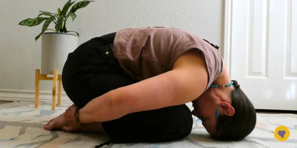 Dawn Browning practices yoga in Child's Pose on a patterned rug indoors, with a potted plant in the background.