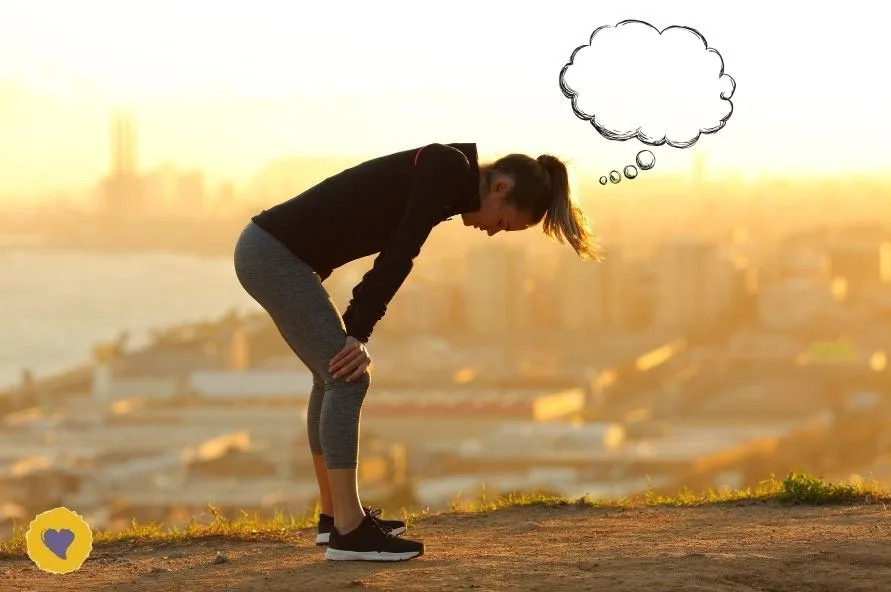 A woman in athletic wear stands on a hill at sunset, bent over with hands on knees, next to a thought bubble urging her to stop thinking about work, overlooking a cityscape.